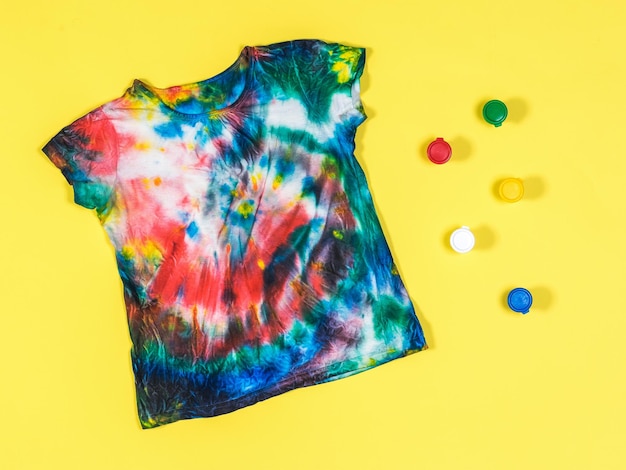 Tie-Dye-T-Shirt und bunte Farbdosen auf gelbem Hintergrund Flach liegend