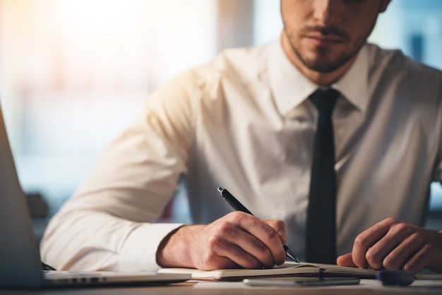 Tief in seiner Arbeit. Nahaufnahme eines jungen Mannes, der in sein Notizbuch schreibt