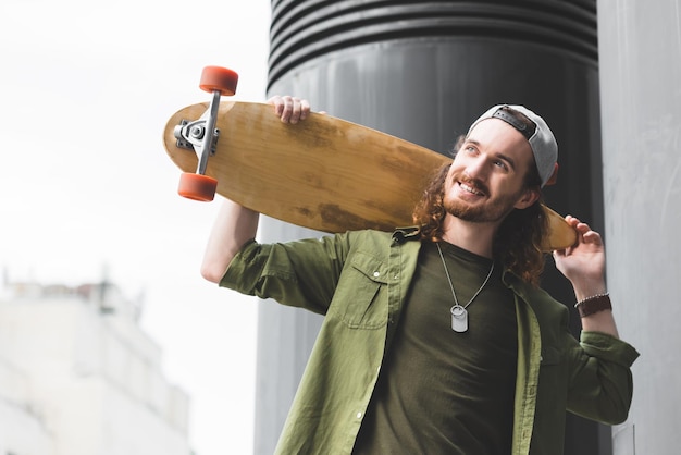 Tiefansicht eines fröhlichen Mannes mit Skateboard, der auf dem Dach steht und wegschaut