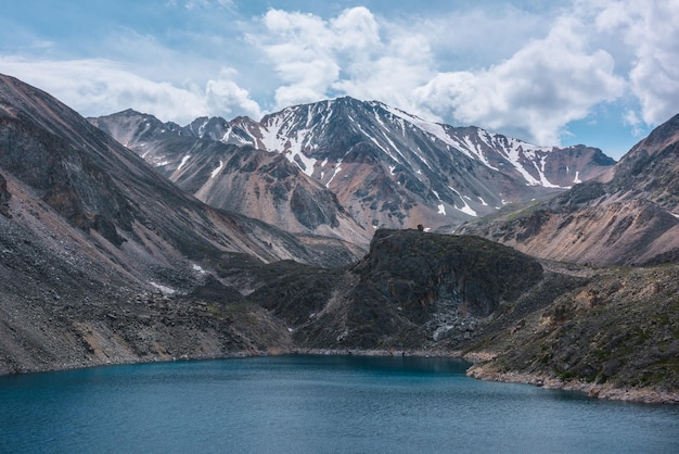 Tiefer Bergsee von phantomblauer Farbe zwischen scharfen Felsen und hohen Bergen bei wechselhaftem Wetter Wundervoller dramatischer Blick auf den tiefblauen Bergsee und die große sonnenbeschienene Felsklippe unter bewölktem Himmel