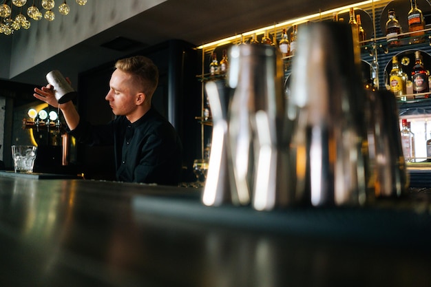 Tiefwinkelansicht eines jungen Barkeepers, der hinter der Bartheke in einem modernen dunklen Nachtclub einen erfrischenden alkoholischen Cocktail zubereitet