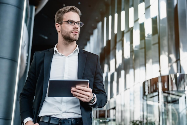 Tiefwinkelansicht eines selbstbewussten jungen Mannes, der an einem digitalen Tablet arbeitet, während er im Business Center steht