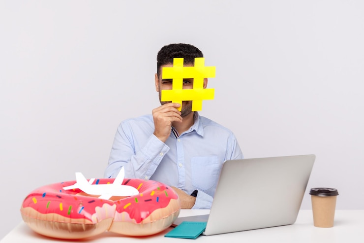 Foto tiempo de descansar. hombre mirando a través del símbolo de hashtag, sentado en el lugar de trabajo de la oficina con pasaporte de anillo de goma y avión de papel en el escritorio, sosteniendo un cartel de hash de un tema web viral sobre viajes relajantes. foto de estudio