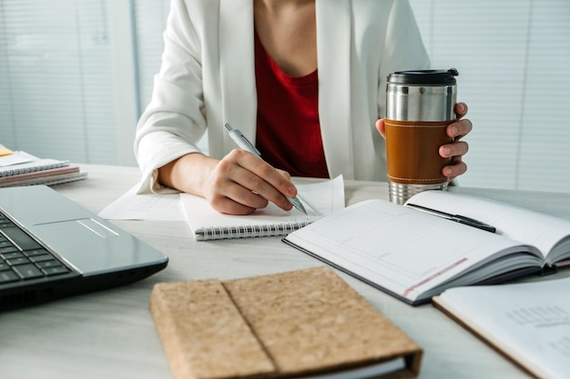 Tiempo de descanso en la oficina cerca de manos de mujer de negocios con taza de café y teléfono celular en el escritorio