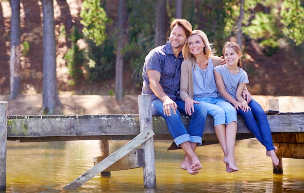 El tiempo en familia es tan precioso Una familia feliz de tres sentados juntos en el embarcadero del lago