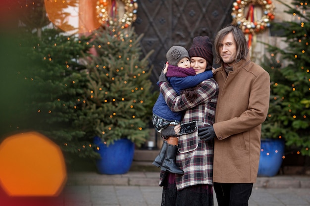 Tiempo de Navidad. Familia feliz: madre, padre y niña caminando en la ciudad y divirtiéndose.