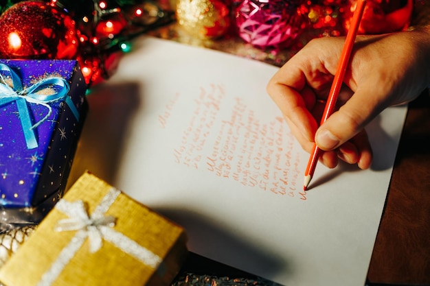 Tiempo de Navidad mano humana escribiendo irreconocible con lápiz rojo sobre papel blanco