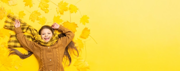 Tiempo de otoño Una niña yace sobre un fondo amarillo entre hojas de arce caídas en otoño Un niño vestido con un cálido suéter de punto y bufanda Copiar espacio