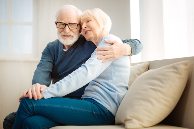 Tiempo con placer. Feliz pensionista mirando a un lado y manteniendo una sonrisa en su rostro mientras abraza a su mujer