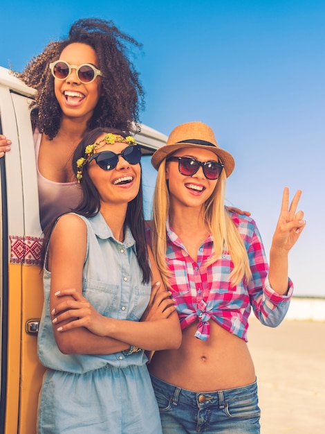 Tiempo sin preocupaciones con amigos. Feliz joven africana mirando desde la minivan retro mientras dos sus amigos de pie cerca de ella