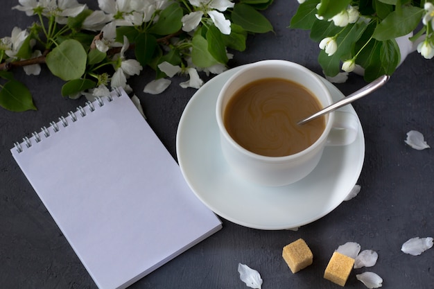 Tiempo relajante y felicidad con una taza de café con flores frescas de primavera. Café de la mañana en un día soleado. Cuaderno con espacio para texto.