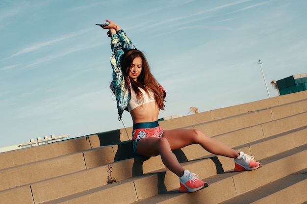 Tiempo para relajarse. Atractiva mujer joven en ropa deportiva sonriendo mientras está sentado en los escalones al aire libre