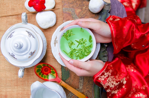 Tiempo de té chino del festival de la luna. Vista superior sobre las manos de la mujer con la taza de té verde en tradi