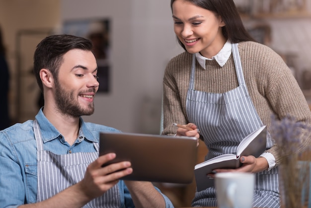 Tiempo de trabajo emocional. Feliz pareja encantadora sonriendo y tomando notas mientras usa la tableta.