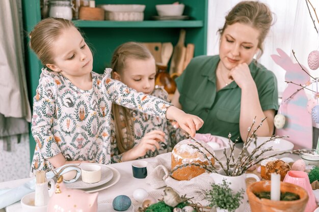 Tiempo de vacaciones de Pascua en la temporada de primavera, familia feliz, sinceros, niños pequeños, hermanas, niñas, juntas, madre, diviértanse en casa decorando la mesa para el almuerzo o la cena, comida tradicional, decoración festiva del hogar.