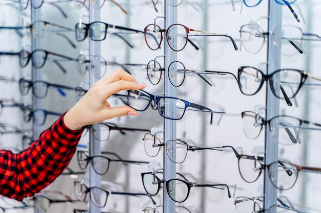 Tienda de anteojos Soporte con anteojos en la tienda de óptica Mano de mujer elige anteojos