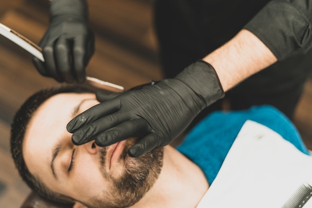 Tienda de belleza para hombres. afeitarse la barba en una barbería. barber  se corta la barba con una navaja y una maquinilla. cerrar cortes de pelo  brutales. equipamiento de peluquería. enfoque selectivo.