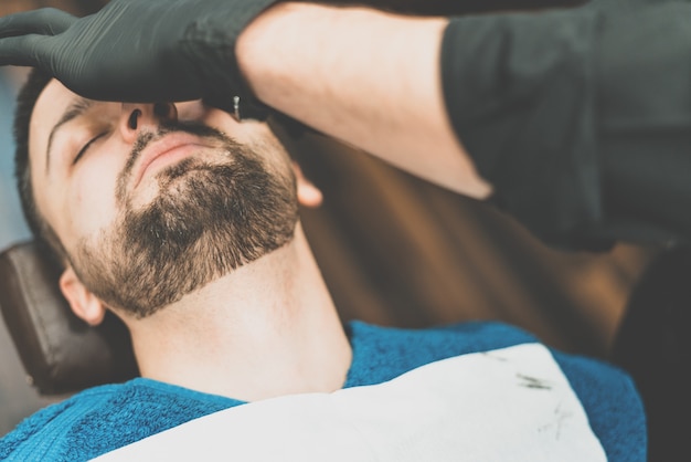 Tienda de belleza para hombres. afeitarse la barba en una barbería. barber se corta la barba con una navaja y una maquinilla. cerrar cortes de pelo brutales. equipamiento de peluquería. enfoque selectivo.