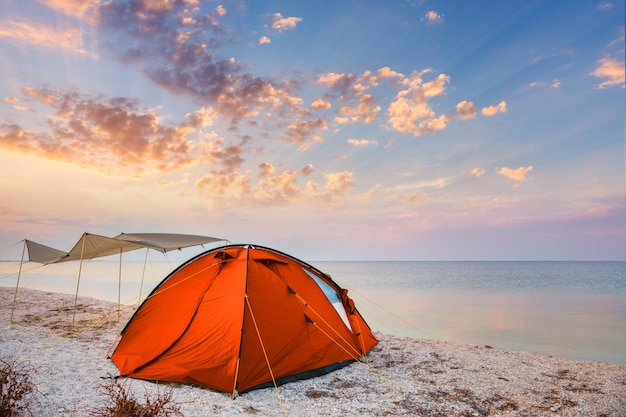 Tienda de campaña en una hermosa playa tranquila cerca del agua contra el fondo del cielo del atardecer feliz verano