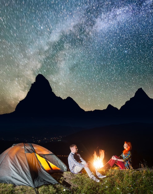 Tienda de campaña nocturna. Turistas sentados junto a la fogata bajo el cielo estrellado