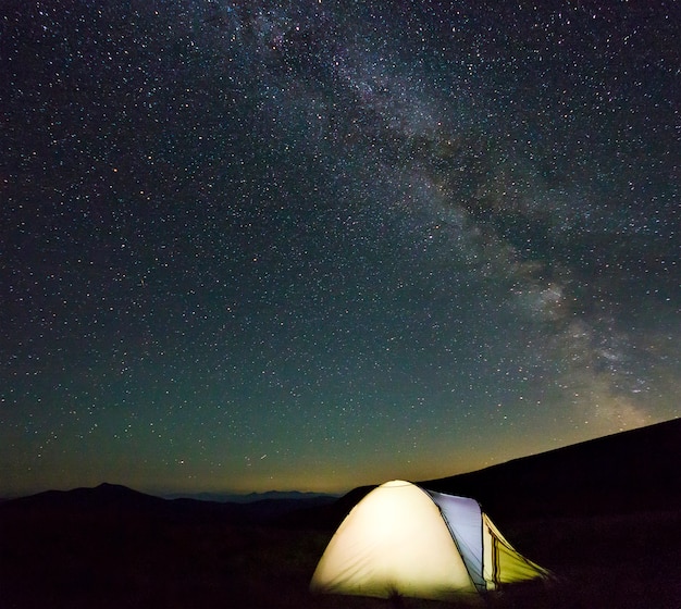 Tienda de excursionistas turísticos en las montañas por la noche con estrellas de la vía láctea en el cielo