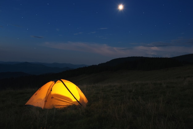 Tienda naranja iluminada en la cima de la montaña por la noche