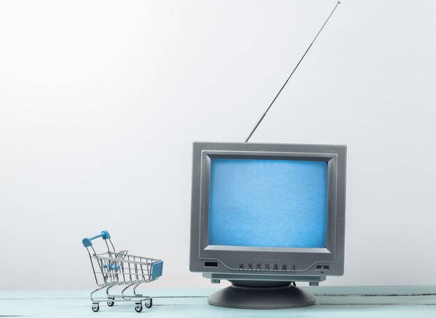 Tienda de TV. Antena de tv retro antigua con mini carro de supermercado en la pared blanca