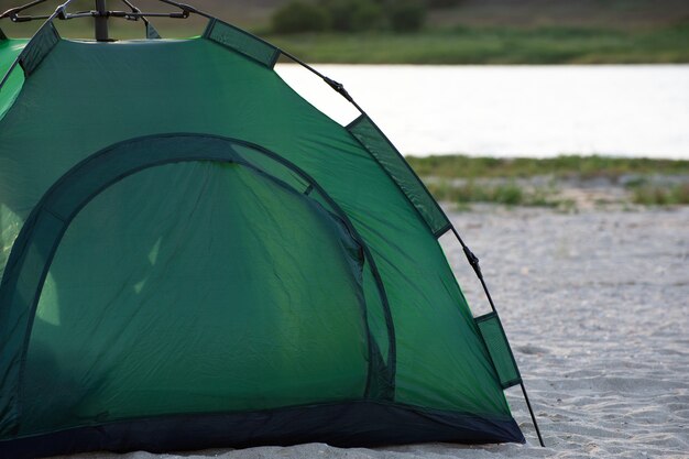 Tienda verde en la playa de arena contra el fondo del río. Camping, trekking, senderismo.