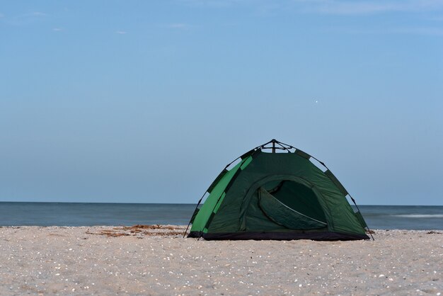 Tienda verde en la playa de arena contra el mar y el cielo azul de fondo. Camping, turismo activo.