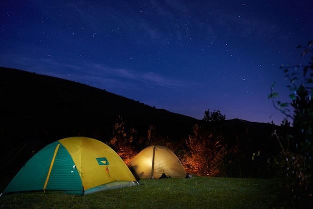 Tiendas de campaña amarillas iluminadas bajo las estrellas por la noche