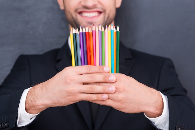 Tiene mente creativa. Close-up de lápices de colores en las manos del empresario sonriente de pie contra la pizarra