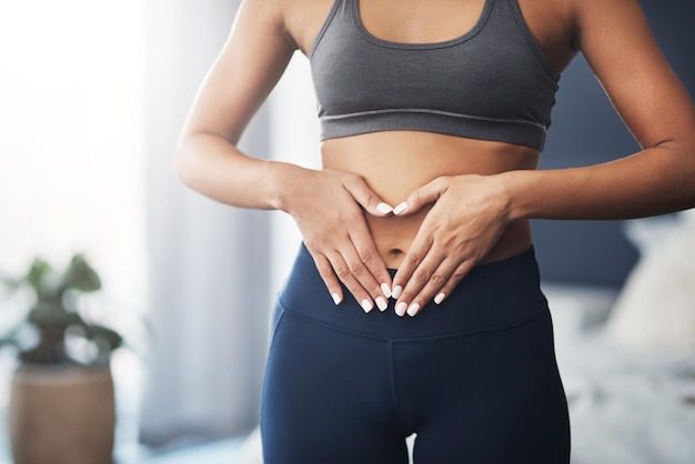 Tienes que mostrar amor a tu cuerpo Captura recortada de una mujer joven irreconocible haciendo una forma de corazón en su estómago en su dormitorio