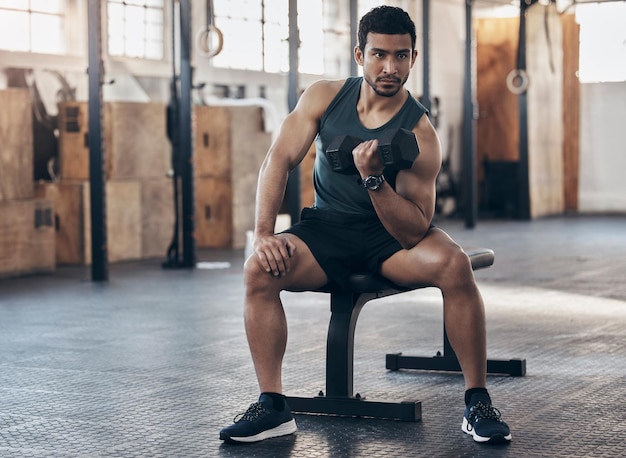 Tienes que romper tu límite. Una foto de un joven musculoso haciendo ejercicio con una mancuerna en un gimnasio.