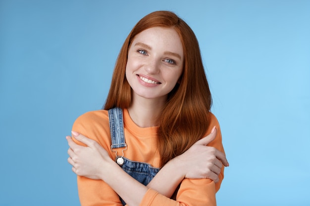 Tierna chica pelirroja tonta de pie fondo azul sonriendo alegremente abrazando los brazos cruzados cuerpo siente frío sonriendo encantado hablando novio cita romántica pidiendo prestar chaqueta fría noche de verano.