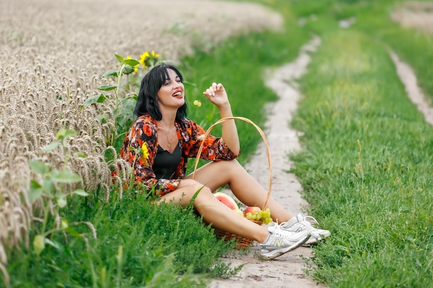 Una tierna y hermosa joven se sienta en un campo de trigo y come uvas