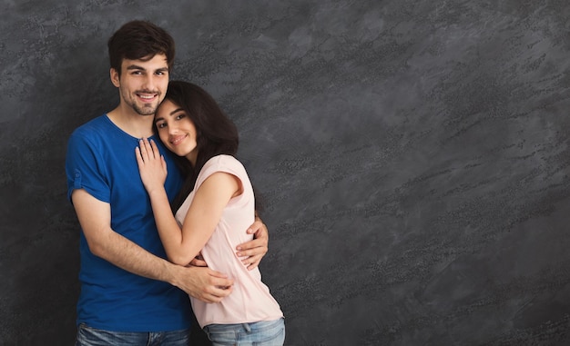 Tierna joven pareja de enamorados abrazándose sobre fondo gris, espacio de copia