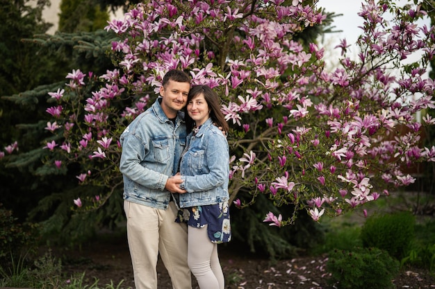 Tierna pareja enamorada usa chaqueta de jeans disfrutando de un agradable día de primavera cerca del árbol floreciente de magnolia