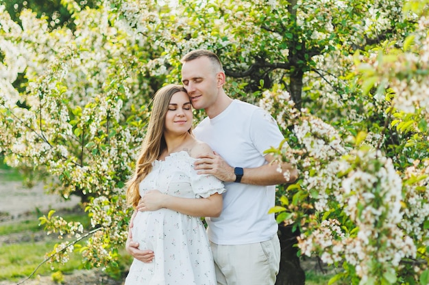 Tierna pareja romántica embarazada abrazándose en el floreciente jardín de primavera de manzanas Futuros padres en el parque de árboles de flores blancas Una pareja espera un bebé