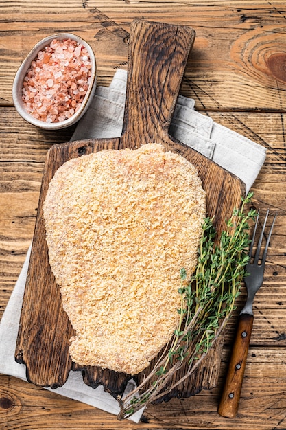 Tierno escalope de salchicha empanizada cruda sobre una tabla de madera con tomillo. fondo de madera. Vista superior.