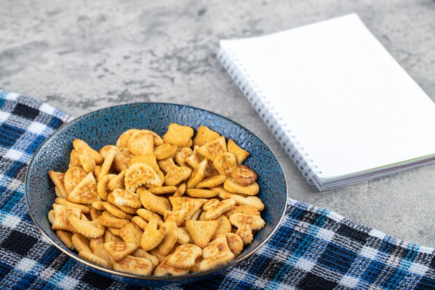 Tigela azul de biscoitos secos salgados e caderno vazio na superfície da pedra.