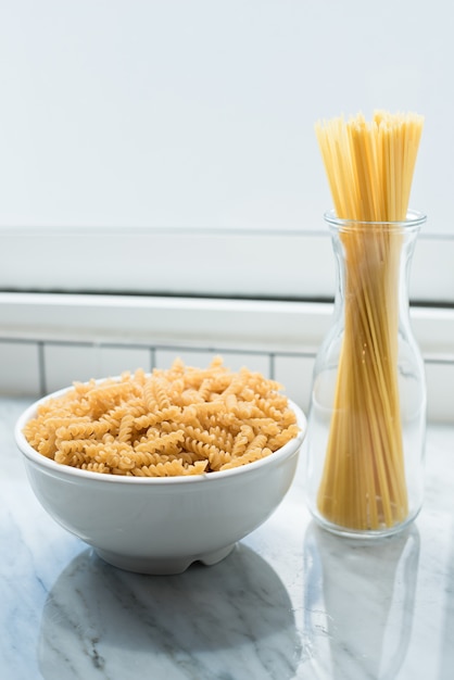 Foto tigela branca de macarrão espiral e espaguete amarrado erguem-se nas janelas da sala da cozinha