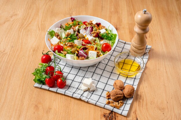 Tigela branca de salada vegetariana com alface americana com uma mistura de ingredientes saudáveis como nozes, cerejas, tomates, nozes, cenouras, queijo fresco e milho. Vista do topo