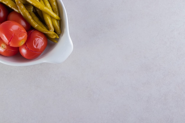 Tigela branca de tomate em conserva e pimentão na mesa de pedra.