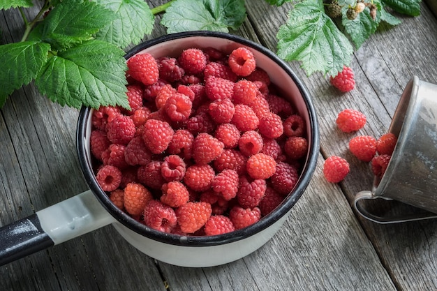 Tigela cheia de framboesas e caneca rústica com frutas maduras espalhadas Vista superior