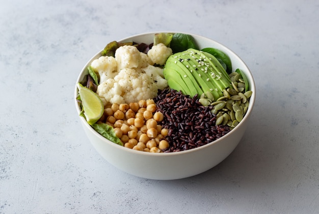 Tigela com abacate, arroz preto, grão de bico, repolho, espinafre e salada. Alimentação saudável. Comida vegetariana.