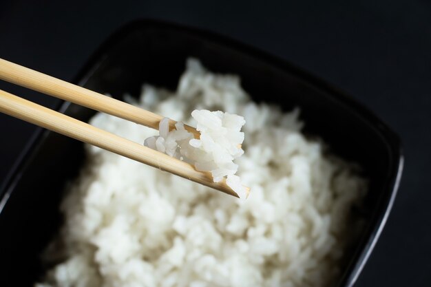 Tigela com arroz cozido em um fundo preto. Comida asiática e pauzinhos de bambu.