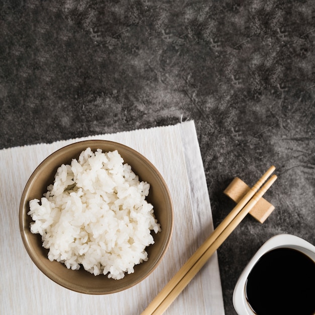 Tigela com arroz no guardanapo perto de pauzinhos e molho de soja