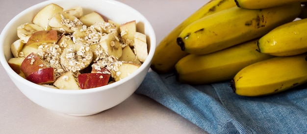 tigela com banana picada e maçã com aveia e cacho de banana madura ao lado em um pano azul