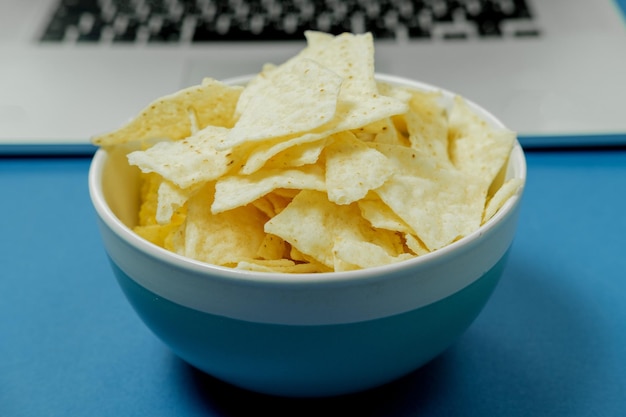 Tigela com batatas fritas em um fundo de laptop em um fundo azul Conceito de maus hábitos
