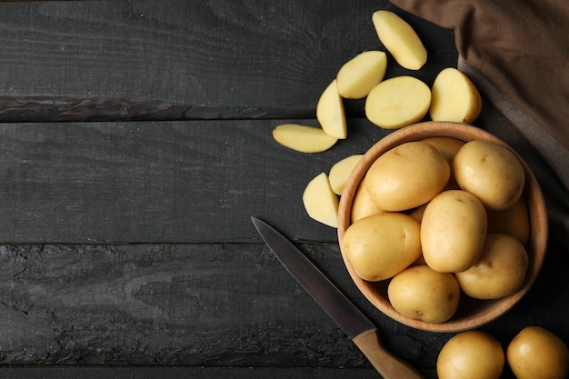 Tigela com batatas jovens, toalha e faca na superfície de madeira